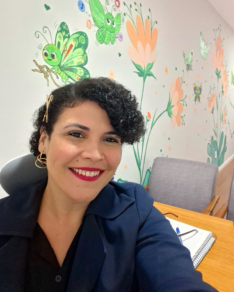 Débora Peres, psicóloga clínica, sorrindo em seu consultório em Rio das Ostras